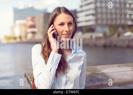 Attraktive Frau, nehmen einen Anruf auf ihrem Handy stehen im Freien vor dem Fluss-Hintergrund Stockfoto