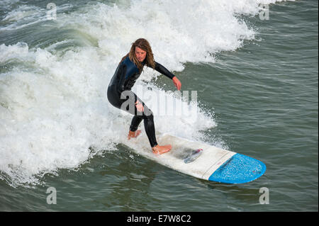 Surfer mit Dreadlocks im schwarzen Anzug auf Surfbrett Welle zu reiten, da es entlang der Nordseeküste bricht Stockfoto