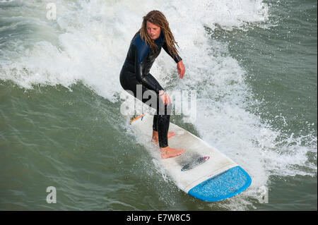 Surfer mit Dreadlocks im schwarzen Anzug auf Surfbrett Welle zu reiten, da es entlang der Nordseeküste bricht Stockfoto