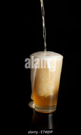 Unbeschriftetes Bier wird in Pint Glas auf schwarzem Hintergrund gegossen Stockfoto