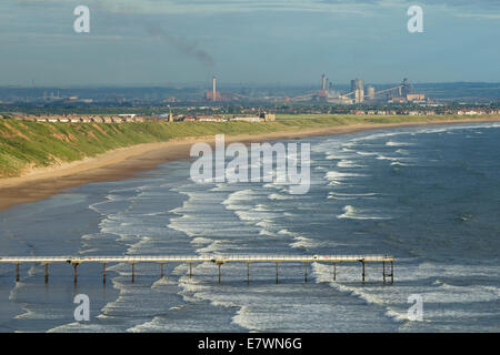 Blick über Saltburn Pier und Strand mit Redcar Stahlwerk in Ferne. Saltburn von Meer, North Yorkshire, England, UK Stockfoto