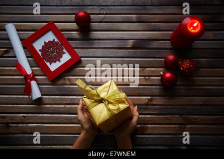 Goldene Geschenkverpackung in weiblichen Händen und Gegenständen Xmas auf hölzernen Hintergrund Stockfoto