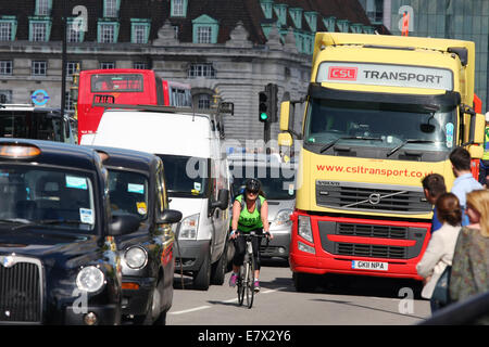 Eine weibliche Radfahrer unter Verkehr in London unterwegs. Fußgänger warten auf die Straße zu überqueren. Stockfoto