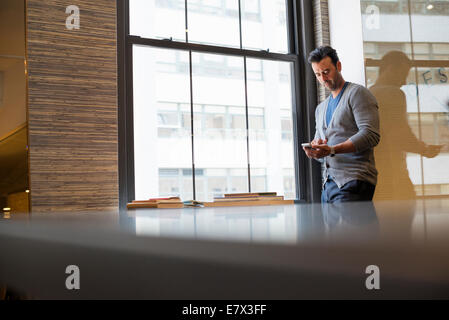 Büroalltag. Ein Mann, der durch ein Fenster in einem Büro Überprüfung seiner Smartphone. Stockfoto
