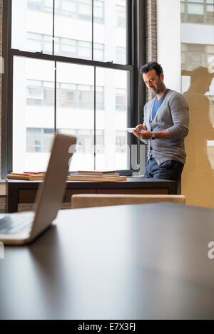 Büroalltag. Ein Mann, der durch ein Fenster in einem Büro Überprüfung seiner Smartphone. Stockfoto