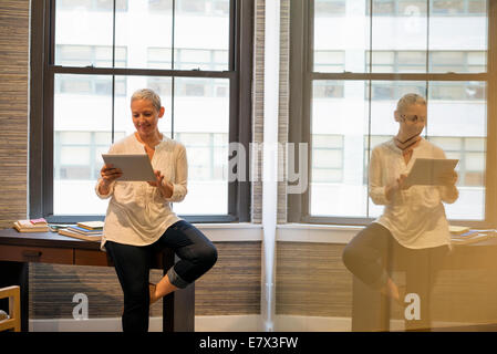 Büroalltag. Eine Frau sitzt am Rande von ihrem Schreibtisch mit einer digital-Tablette. Stockfoto
