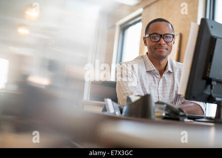 Büroalltag. Ein Mann sitzt an einem Schreibtisch mit einem Computer. Stockfoto