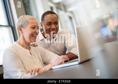 Büroalltag. Zwei Menschen, Mann und Frau ein Laptop-Bildschirm betrachten und lachen. Stockfoto