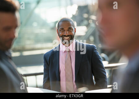 Ein Business-Mann sitzt lächelnd souverän, in einer Gruppe mit zwei anderen. Stockfoto