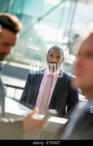 Ein Business-Mann sitzt lächelnd souverän, in einer Gruppe mit zwei anderen. Stockfoto