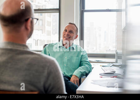 Zwei Männer sitzen in einer hellen luftigen Büroumgebung sprechen. Stockfoto
