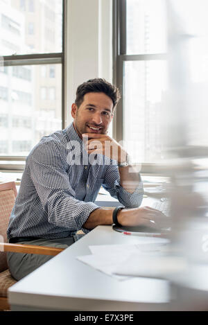 Büroalltag. Ein Mann sitzt an einem Schreibtisch in die Kamera schaut. Stockfoto