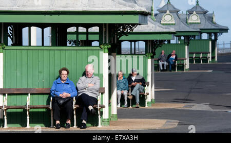 Ältere Paare sitzen auf Bänken in einer Reihe von Unterkünften auf der Promenade in Blackpool Stockfoto