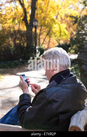 Senior-Mann-SMS auf dem iPhone im Central Park im Herbst, NYC Stockfoto