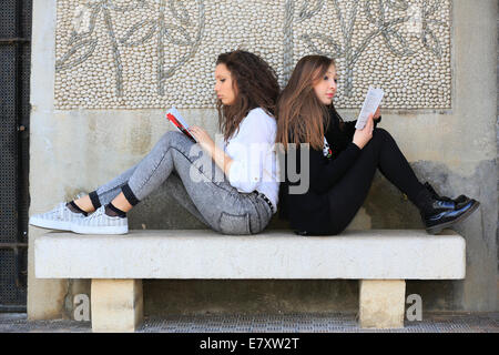 Zwei Freundinnen, Teenager, sitzen Rücken an Rücken auf einer Steinbank, Lesebücher, Menton, Alpes-Maritimes, Provence-Alpes Stockfoto