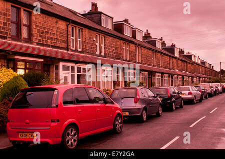 Durchgehende Linie der geparkten Autos außerhalb einer langen Geraden Terrasse aus Stein gebaute Häuser unter einem Rosa Rot sonnenuntergang himmel - Burley in Bösingen, Yorkshire, Großbritannien Stockfoto