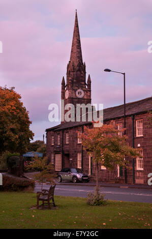 Rosa Rot sonnenuntergang himmel über Village Green, Reihe von traditionellen Cottages & Turm von St. Mary's Church - Burley in Bösingen, West Yorkshire, England, UK. Stockfoto