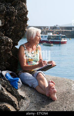 Reifen Fit gesunde aktive weibliche Künstlerin zeichnen / skizzieren ein Skizzenbild. Mevagissey Hafenbucht / Stadt. Cornwall UK Stockfoto