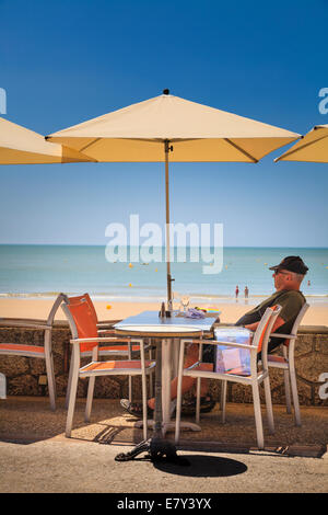 Ein Mann sitzt unter Dach am Café-Tisch von Strand. Stockfoto