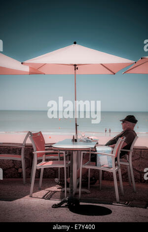 Ein Mann sitzt unter Dach am Café-Tisch von Strand Instagram Behandlung. Stockfoto