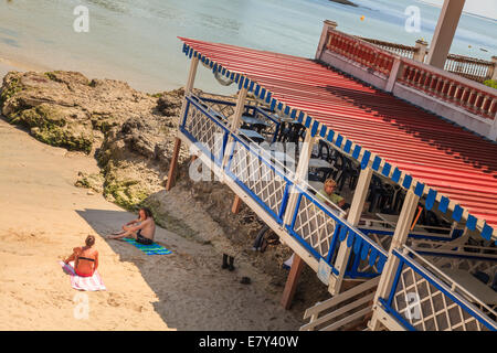 Strandrestaurant auf Stelzen und zwei Sonnenanbeter auf Handtücher für den Strand. Stockfoto