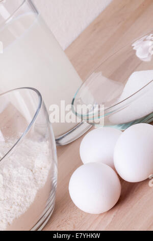 Zutaten in der Küche mit einer Schüssel Mehl, Eier, Zucker, Krug mit Milch und Butter bereit, einen Kuchen backen oder Teig backen Stockfoto