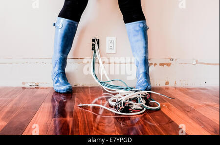 Frau trägt Galoschen stehend über elektrische Verdrahtung Stockfoto