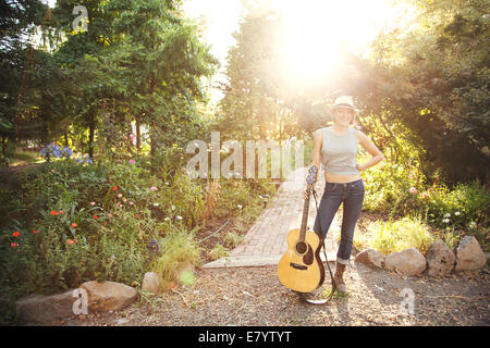 Junge Frau mit akustischer Gitarre im Garten Stockfoto