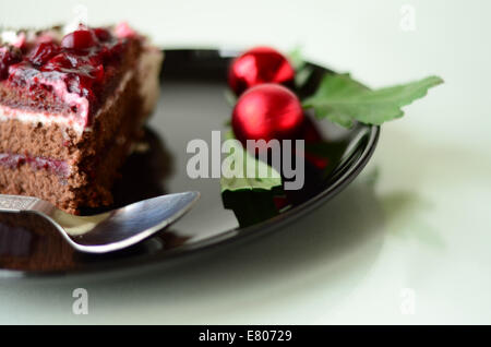 Schwarzwälder Torte Stück in eine schwarze Platte mit Weihnachtsdekoration und einen Löffel Stockfoto