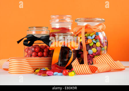 Candy in Glas Gläser mit Orangen und weißen Streifen Band für Halloween oder Partei begünstigt. Stockfoto