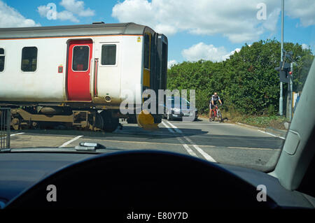 Auto- und Radfahrer warten an einer offenen Bahnübergang, Melton, Suffolk, UK. Stockfoto