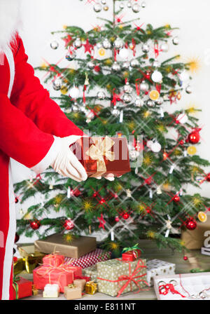 Weihnachtsmann mit Geschenk in der hand vor einem Weihnachtsbaum steht Stockfoto