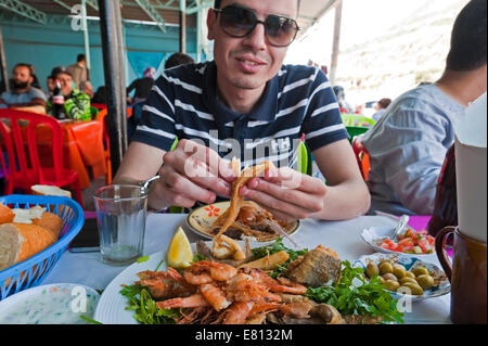 Horizontale Porträt einer jungen marokkanischen Mann essen Meeresfrüchte mit seinen Händen. Stockfoto