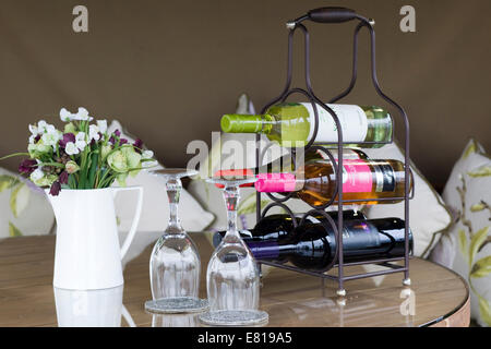 Rack mit verschiedenen Weinen und zwei Weingläser mit Krug mit Blumen auf einem Esstisch Stockfoto