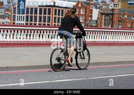 Eine weibliche Radfahrer, mit einer Tasche auf ihrem Lenker, Radfahren über Waterloo Bridge in London Stockfoto