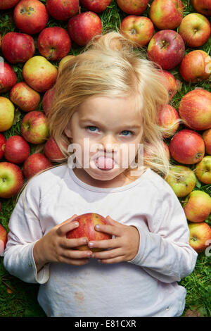 kleines Mädchen auf dem Rasen liegend mit grün rote Äpfel Stockfoto