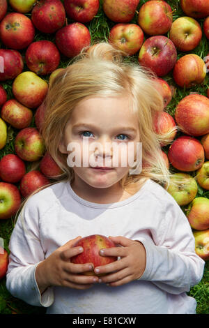 kleines Mädchen auf dem Rasen liegend mit grün rote Äpfel Stockfoto