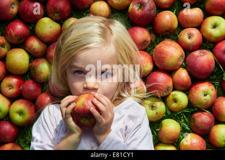 Porträt von Kind blondes junges Mädchen liegen und Essen auf dem Rasen mit Äpfeln Hintergrund, liegt Stockfoto