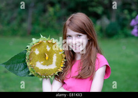 Mädchen hält eine Sonnenblume (Helianthus Annuus) mit einem lächelnden Gesicht Stockfoto