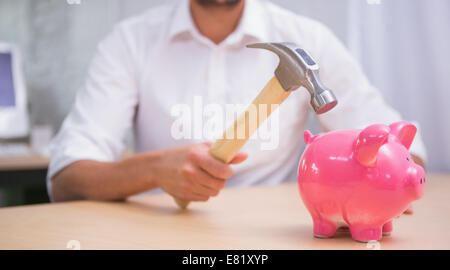 Mann bricht Sparschwein mit hammer Stockfoto