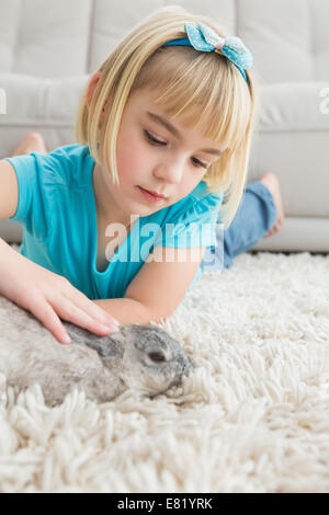 Kleines Mädchen liegend auf Teppich die Kaninchen streicheln Stockfoto