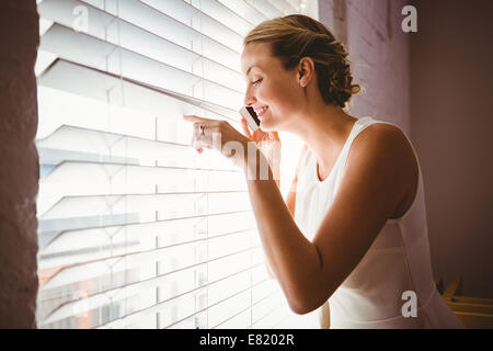 Lässige Geschäftsfrau mit Handy beim Blick durch Jalousien Stockfoto