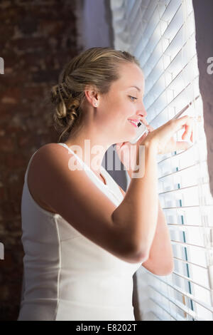 Lässige Geschäftsfrau mit Handy beim Blick durch Jalousien Stockfoto