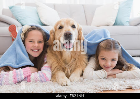 Schwestern auf Teppich mit golden Retriever unter einer Decke liegen Stockfoto