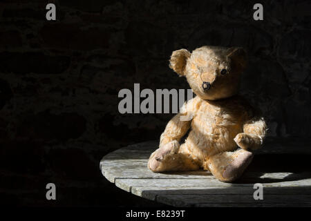 Alten fadenscheinig One Eyed Teddy saß auf einem Holztisch im Sonnenlicht Stockfoto