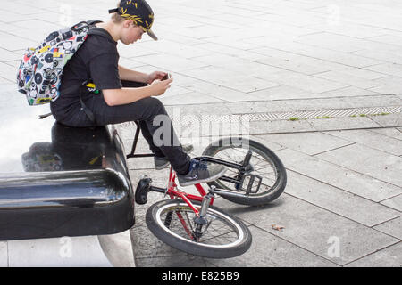 Ein junger Teenager befasst sich mit einem Smartphone sitzend mit seinem Motorrad In Sheffield UK Stockfoto