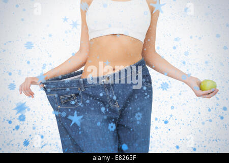 Mittelteil der schlanke Frau trägt zu groß Jeans hält einen Apfel Stockfoto