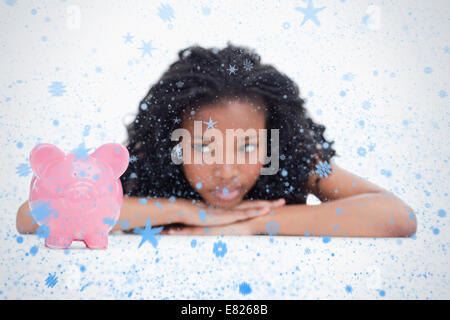 Junge Frau im liegen den Kopf auf den Händen ruhen blickt auf ein Sparschwein Stockfoto