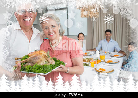 Großeltern mit Hähnchen braten mit Familie am Esstisch Stockfoto