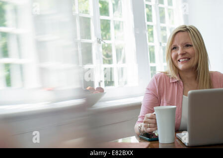 Eine Frau mit einem Laptop an einem Tisch zu Hause arbeiten. Stockfoto